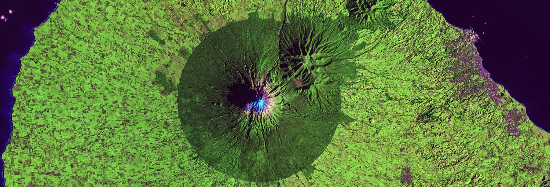 False-color aerial image of a circular volcanic caldera ringed by vegetation.